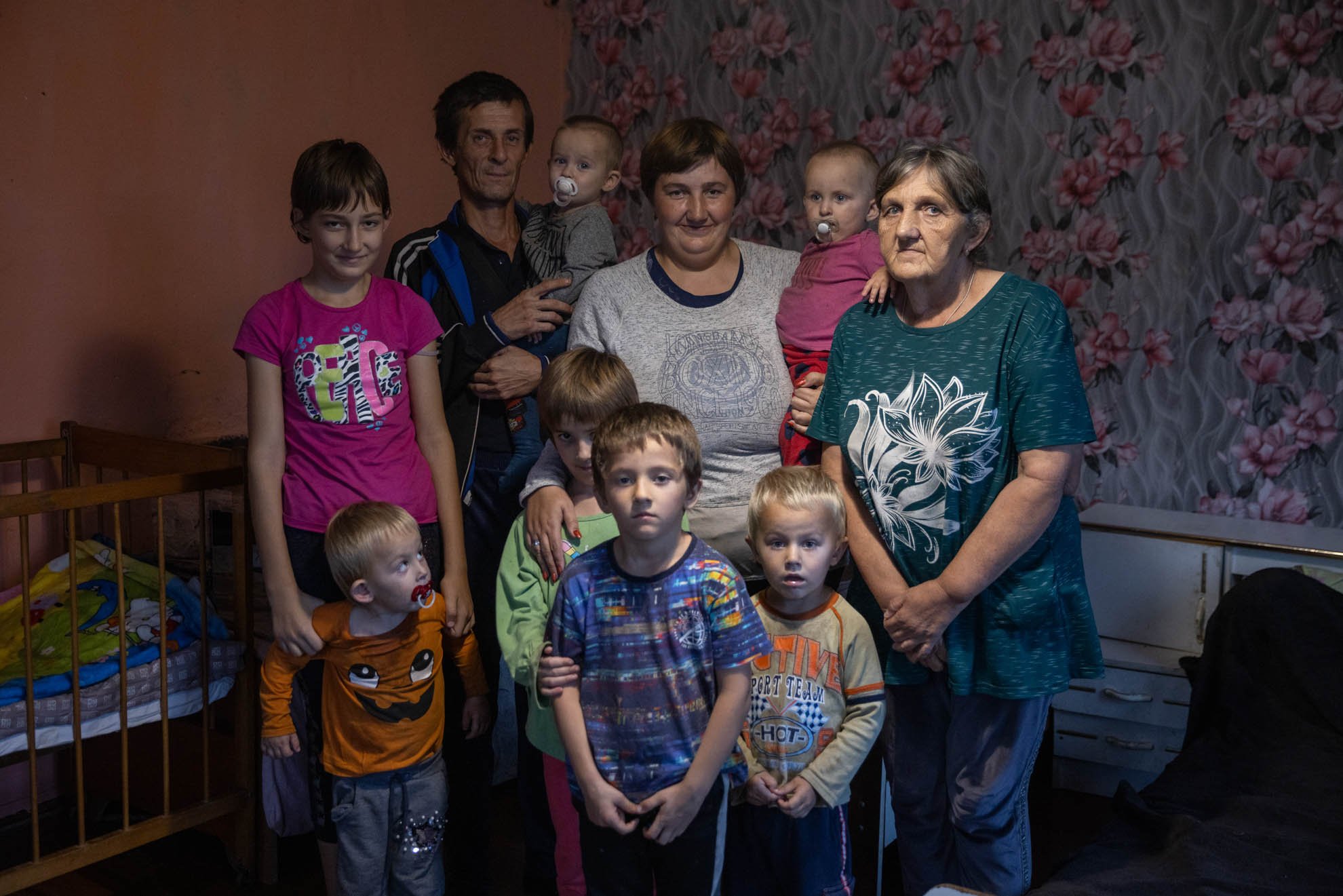 Olha, Volodymyr and their family are standing up and posing for a photo in their bedroom. 
