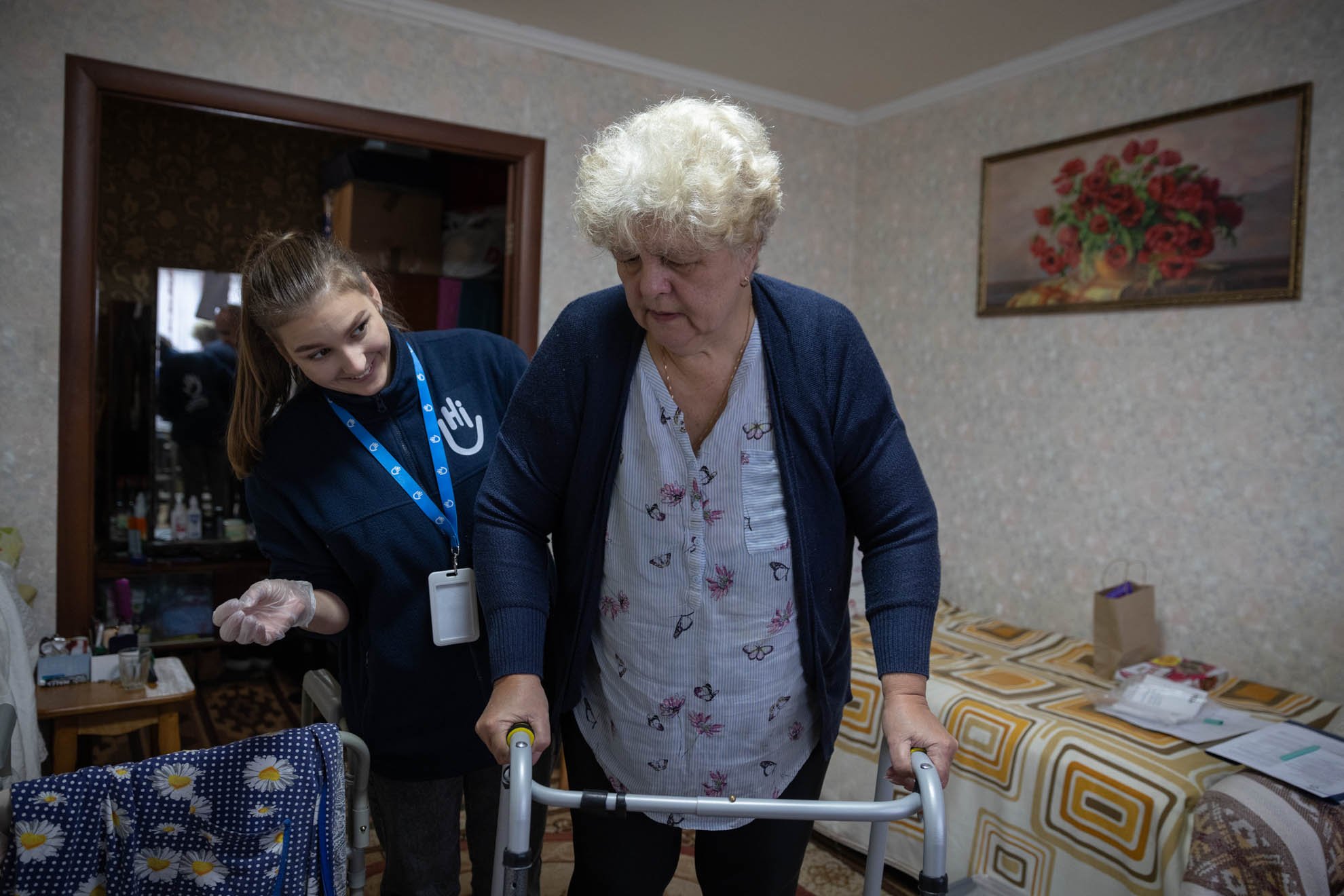 HI’s staff is smiling at Antonina while she is using her walker in her house.